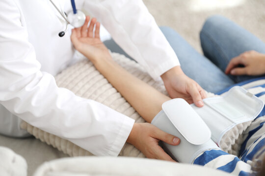 Doctor checking woman's heart rate and blood pressure via sphygmomanometer on sofa indoors, closeup - Powered by Adobe