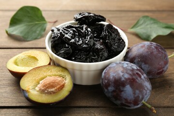 Dried prunes, fresh plums and green leaves on wooden table, closeup