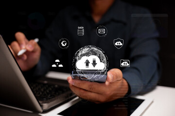 A person using a smartphone to interact with cloud computing icons, symbolizing data transfer and technology in a dark setting.