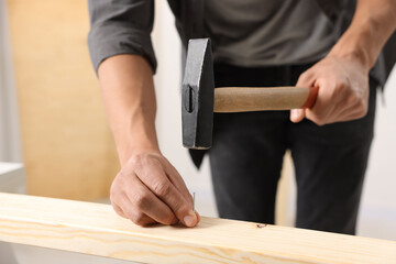 Man hammering nail into wooden plank indoors, closeup