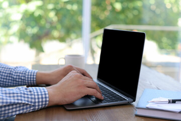 Man working on laptop at wooden table indoors, closeup