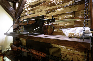 Rifles are displayed on rustic wooden shelves against a textured stone wall. Chains suspend the shelves, adding to the vintage aesthetic