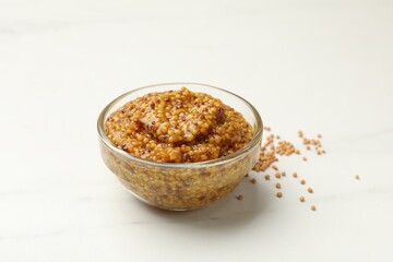 Whole grain mustard in bowl on white marble table, closeup