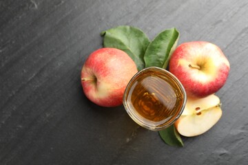 Fresh cider in glass, apples and green leaves on black table, flat lay. Space for text