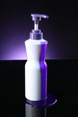 Bottle of hair care cosmetic products for blonde hair on black mirror surface against dark purple background