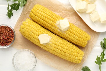 Tasty boiled corncobs with butter, parsley and spices on white wooden table, flat lay