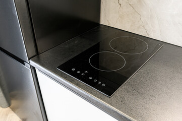 Close-up of a modern induction cooktop set into a gray countertop, adjacent to a gray refrigerator...