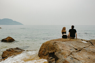 Young caucasian couple sitting on rocks by the ocean with misty horizon