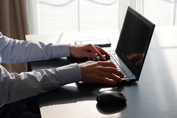 One man working on laptop with computer privacy filter on the screen and smartphone nearby in bright light. Protection of professional secrecy.