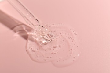 Dripping cosmetic product from pipette on pink background, closeup