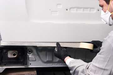 Mechanic covering car with duck tape before painting in auto repair service