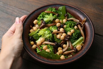 Woman with delicious salad with shimeji mushrooms at wooden table, closeup