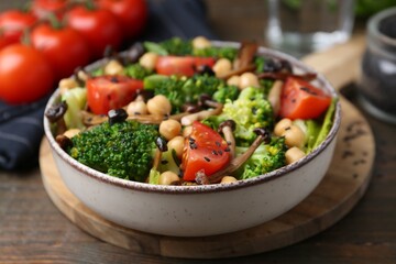 Delicious salad with shimeji mushrooms, chickpeas, tomatoes and broccoli on wooden table, closeup