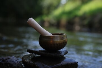 Tibetan singing bowl with mallet on stone near river