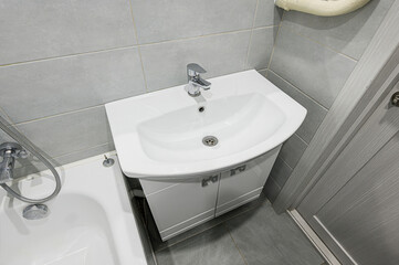 A bathroom interior featuring a white sink with a cabinet, gray tiles on the wall, and a gray door