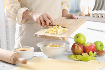 Making delicious apple strudel. Woman putting pieces of fruit into bowl at white marble table in kitchen, closeup