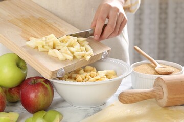 Making delicious apple strudel. Woman putting pieces of fruit into bowl at white marble table in kitchen, closeup