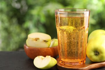 Delicious cider in glass and apples on black table outdoors, closeup