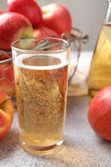 Delicious cider in glass and apples on light grey table, closeup