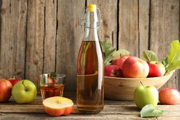 Delicious cider in bottle, glass and apples on wooden table