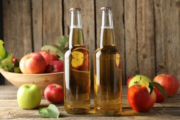 Delicious cider in glass bottles and apples on wooden table