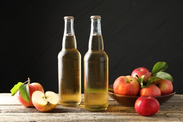 Delicious cider in glass bottles and apples on wooden table against dark gray background