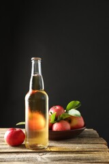 Delicious cider in glass bottle and apples on wooden table against dark gray background