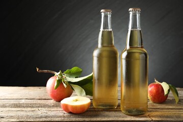 Delicious cider in glass bottles and apples on wooden table against dark gray background. Space for text