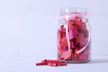 Colorful paper pieces in glass jar on white table, space for text. Message notes