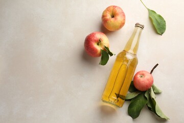 Delicious cider in glass bottle and apples with green leaves on beige table, flat lay. Space for text