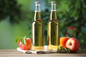 Delicious cider in glass bottles and apples on wooden table outdoors