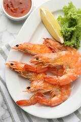 Tasty grilled shrimps served with lemon, lettuce and sauce on white marble table, flat lay. Delicious seafood dish