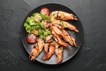 Tasty grilled shrimps served with salad on black table, top view. Delicious seafood dish
