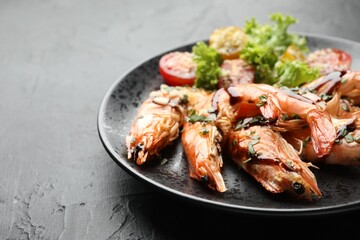 Delicious seafood dish. Tasty grilled shrimps served with salad on black table, closeup. Space for text