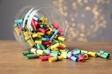 Obraz na płótnie Canvas Colorful paper notes in glass jar on wooden table against grey background with blurred lights, closeup. Bokeh effect
