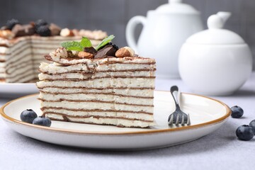 Piece of tasty crepe cake with cocoa powder, chocolate, nuts and blackberry served on light table, closeup