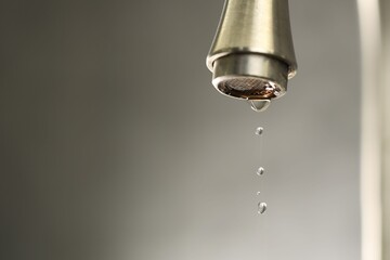Water saving concept. Water dripping from tap on grey background, closeup. Space for text