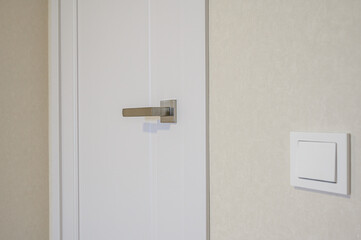 A white door with a metal handle and a white light switch on a beige wall