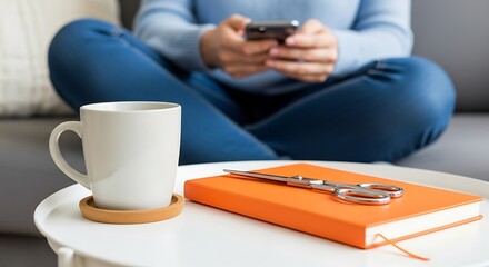 Woman sitting crosslegged on sofa using smartphone with coffee and notebook on table