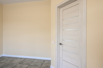 Interior shot of a modern room featuring a sleek, light wood door with glass accents, set against pale yellow walls and a tiled floor