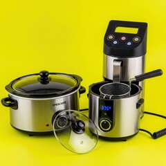 Collection of modern kitchen appliances including a slow cooker deep fryer and sous vide cooker against a bright yellow background