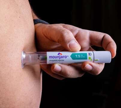 Hand is holding a pre-filled injection pen labeled Mounjaro (tirzepatide injection)