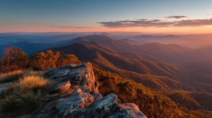 A breathtaking sunset unfolds from a mountain peak, illuminating the rolling hills and valleys with vibrant orange and pink hues. The serene landscape invites tranquility and wonder.