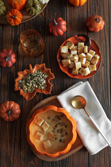 Creamy pumpkin soup with croutons and seeds, served in a pumpkin-shaped bowl on dark wooden table. Top view
