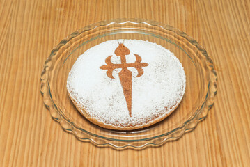 Tarta de Santiago decorated with the stylized Cross of St. James and surrounded by toasted flaked almonds, on a traditional lace paper base
