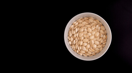 Pumpkin seeds in bowl of water, view from above on black background with copy space.
