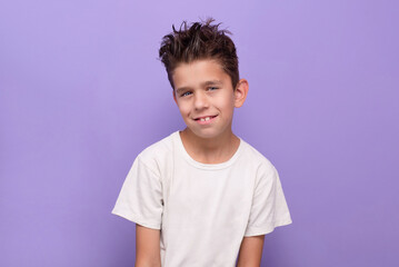 The young boy is self-satisfied, self-confident, handsome with modern hairstyle. A young boy smiles confidently while wearing a white shirt with a purple background, showcasing youthful joy