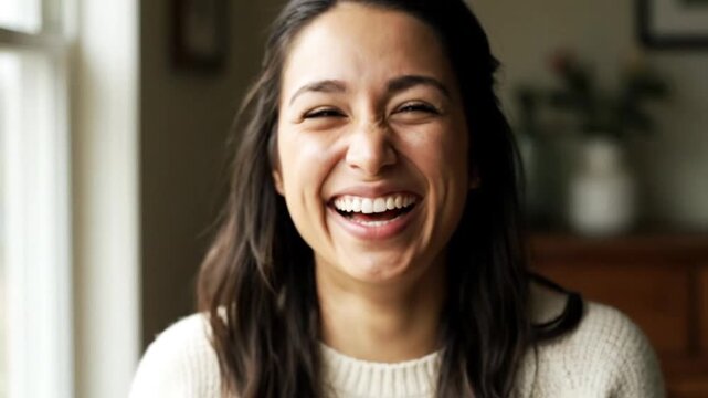 Authentic close-up portrait of a cheerful young woman with a radiant smile bursting into sincere laughter showcasing happiness and positive energy in a warm ind