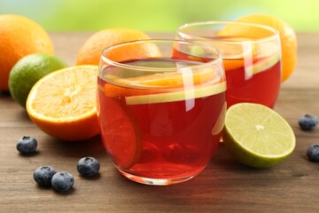 Tasty punch with fruits and blueberries on wooden table against blurred green background, closeup. Refreshing drink