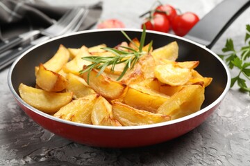 Tasty baked potatoes with rosemary in frying pan on grey textured table, closeup